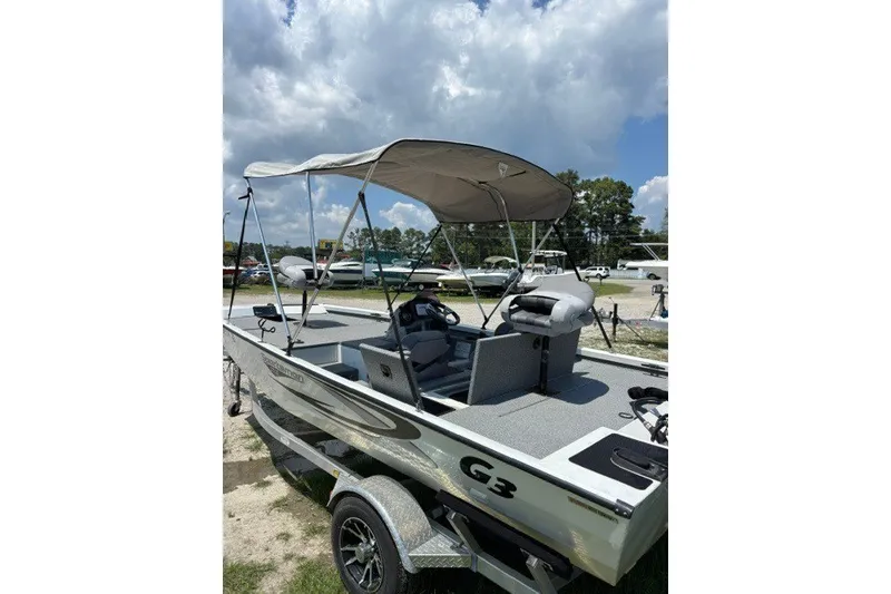 Slide: The Image of 2022 G3 Sportsman 1710 PFX boat with canopy, parked outdoors under a cloudy sky. - 19