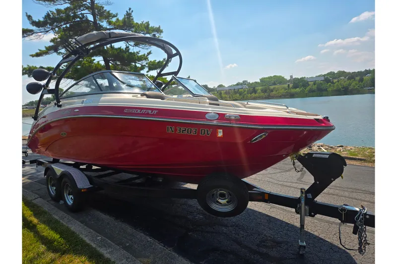 Slide: The Image of 2014 Yamaha Boats 242 Limited S in red, parked on a trailer by a lakeside. - 8