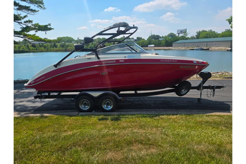 Slide: The Image of 2014 Yamaha Boats 242 Limited S in red, parked by a serene lake. - 9