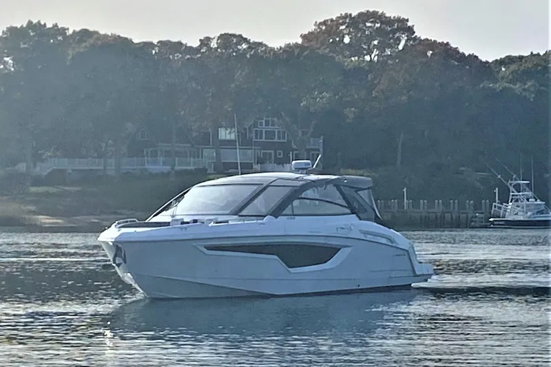 Slide: The Image of 2026 Cruisers Yachts 42 GLS OB on calm water near a wooded shoreline. - 2
