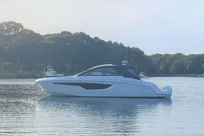 The Image of 2026 Cruisers Yachts 42 GLS OB on serene water with forested background. - 1