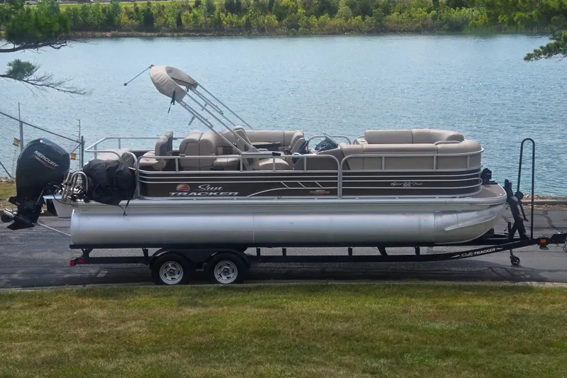 The Image of 2023 Sun Tracker SportFish 22 DLX pontoon boat on trailer by a lake. - 0