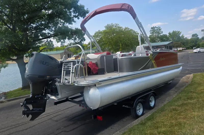 Slide: The Image of 2024 Avalon LSZ Cruise Bench pontoon boat on trailer, parked near a lake. - 1