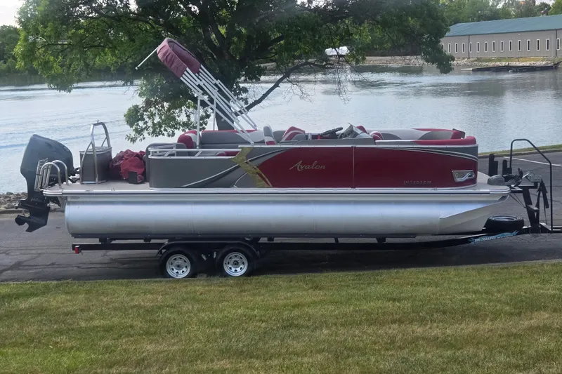The Image of 2024 Avalon LSZ Cruise Bench pontoon boat on trailer by a scenic lake. - 0