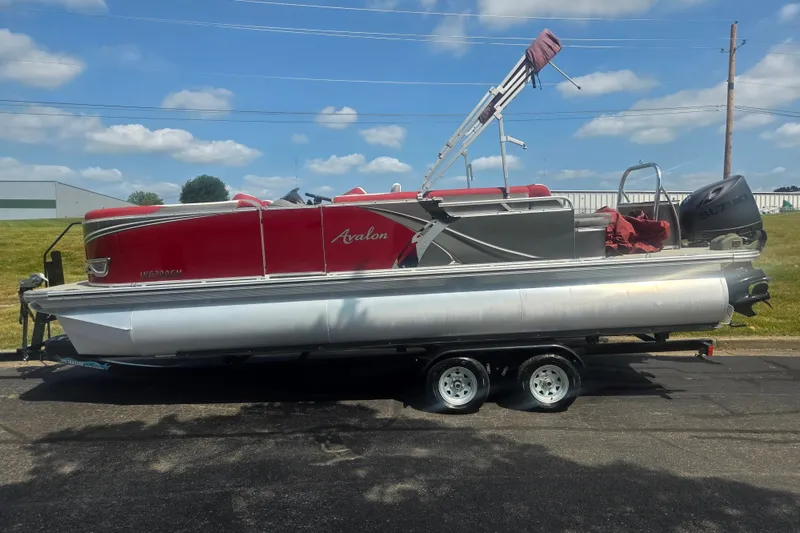 Slide: The Image of 2024 Avalon LSZ Cruise Bench pontoon boat on trailer, red and silver design, parked outdoors. - 4