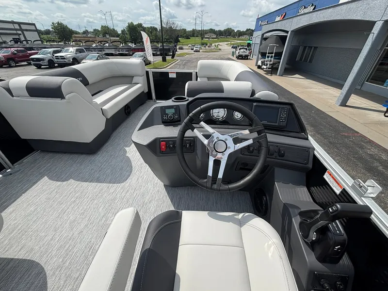 Slide: The Image of The image shows the cockpit of a 2027 Bennington 22 S1SR SPS boat. It features a modern steering wheel, instruments, and comfortable seating. Other boats and a parking lot are visible in the background. - 19