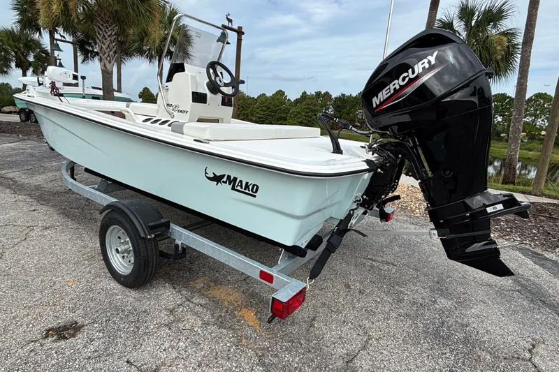 Slide: The Image of 2026 Mako Pro Skiff 13 CC boat with Mercury engine on trailer, parked outdoors. - 2