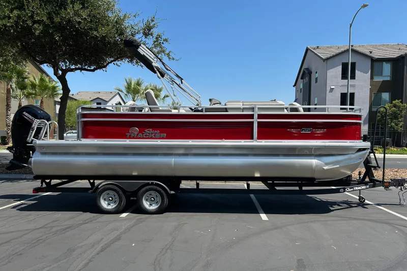 The Image of 2026 Sun Tracker Fishin' Barge 22 DLX pontoon boat on trailer, parked outdoors. - 0