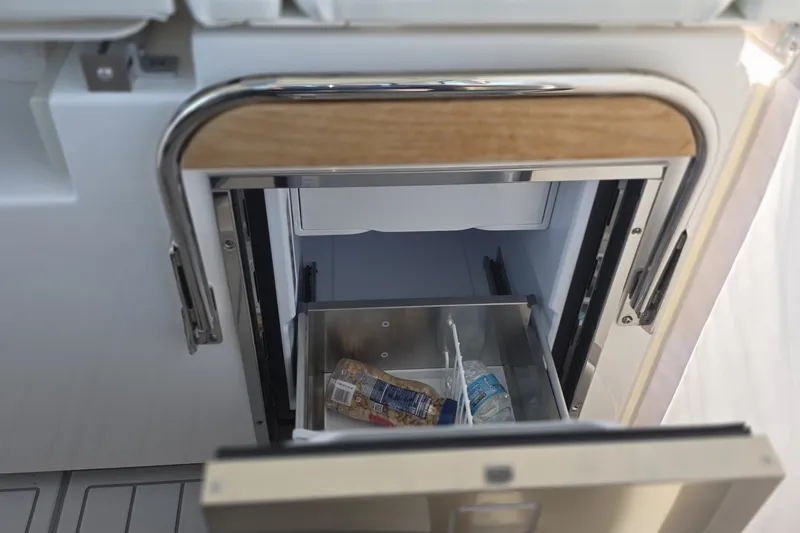 Slide: The Image of Open storage compartment on 2024 Tiara Sport 34LS boat, featuring a drawer with snacks and a water bottle. - 22