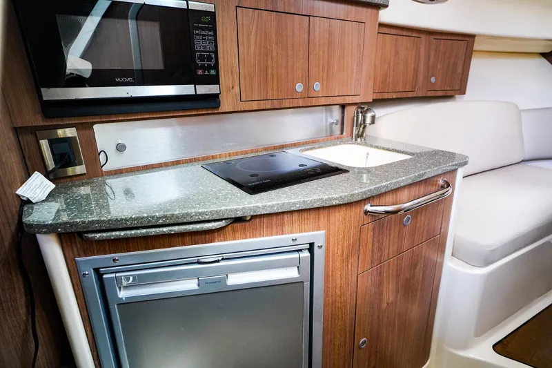 Slide: The Image of 2018 Boston Whaler 315 Conquest interior kitchen with microwave, stove, sink, and fridge. - 23