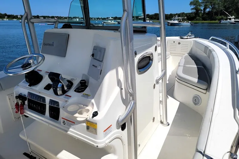 Slide: The Image of 2018 Mako 284 Center Console boat interior with steering wheel and seating, docked by the water. - 21