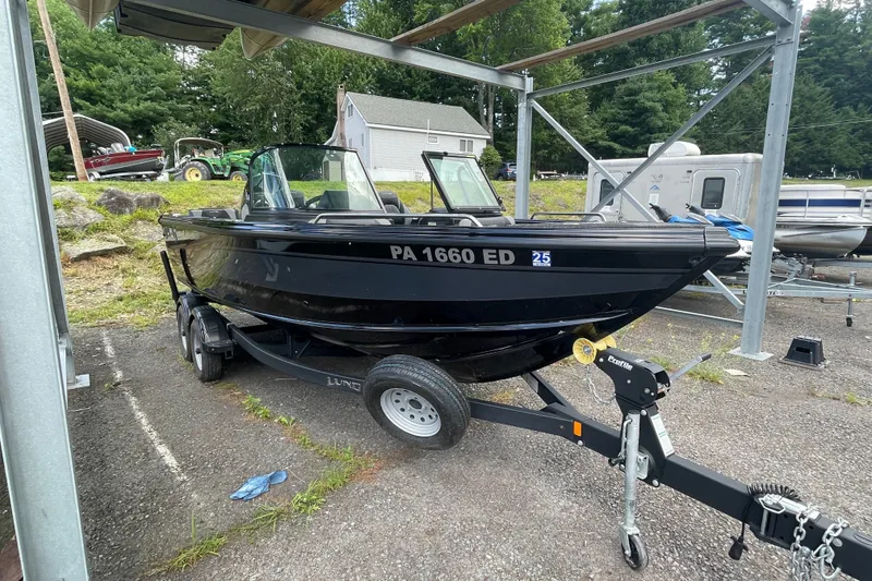 Slide: The Image of Black 2023 Lund 1975 Tyee boat on trailer, parked outdoors near trees and buildings. - 9