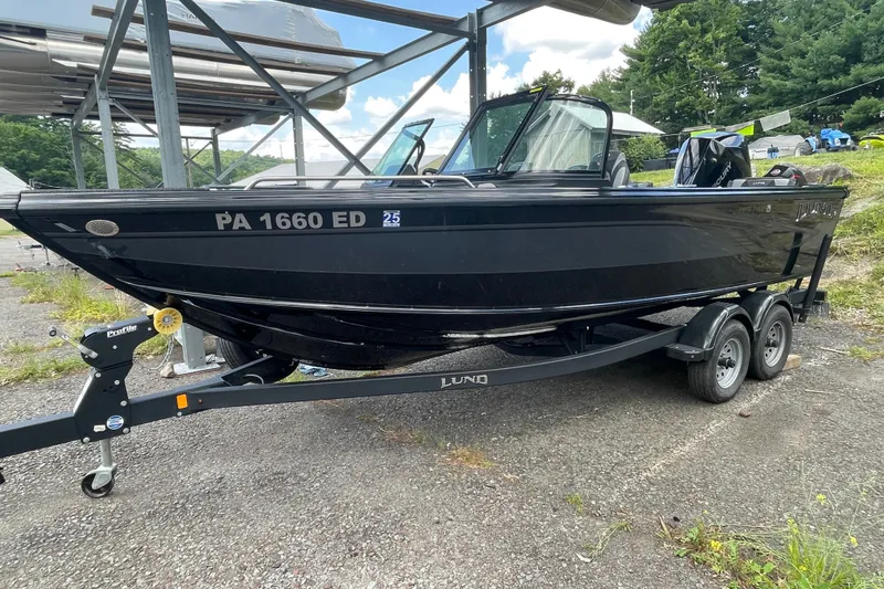 Slide: The Image of Black 2023 Lund 1975 Tyee boat on trailer, parked outdoors under a metal structure. - 10