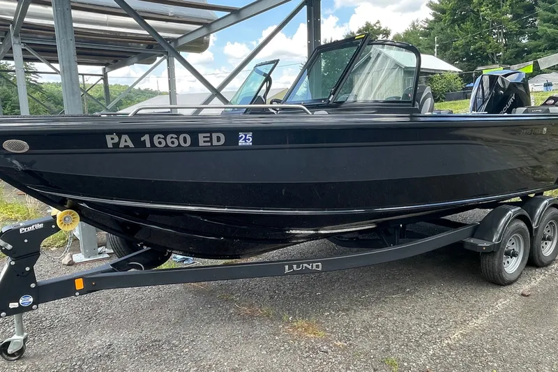 Slide: The Image of Black 2023 Lund 1975 Tyee boat on trailer, parked outdoors under a metal structure. - 1