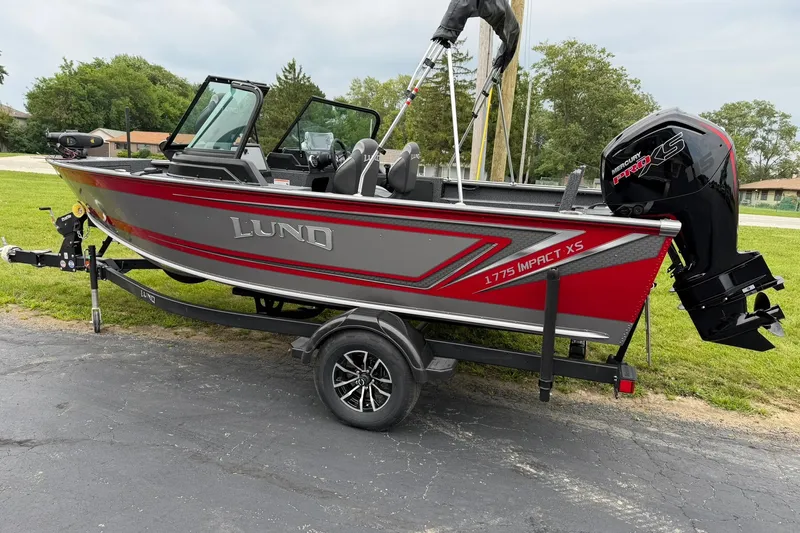 Slide: The Image of 2027 Lund 1775 Impact XS Sport boat on trailer, red and gray design, parked outdoors. - 28