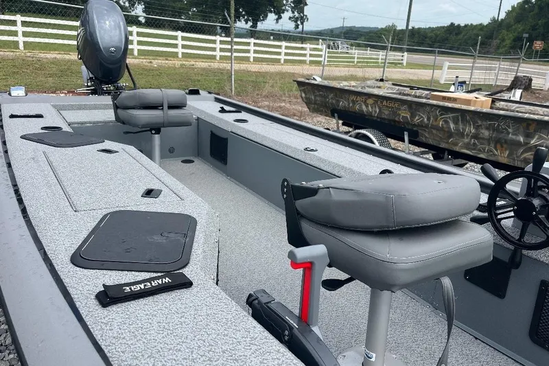 Slide: The Image of 2027 War Eagle 754VS Stick Steer boat with gray seating and steering wheel, parked outdoors. - 4