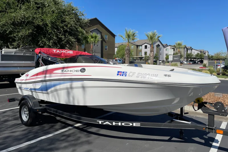 Slide: The Image of 2024 Tahoe T16 boat on trailer, parked outdoors with residential buildings in background. - 2