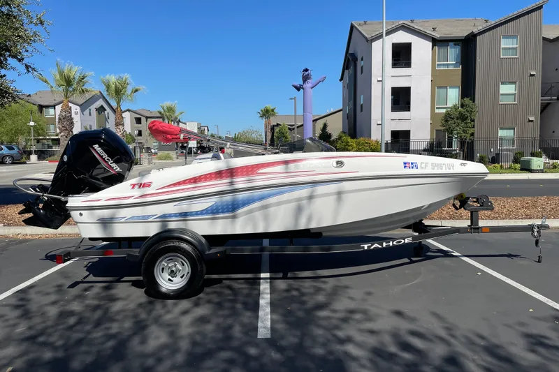 The Image of 2024 Tahoe T16 boat on trailer in parking lot, with modern buildings in background. - 0