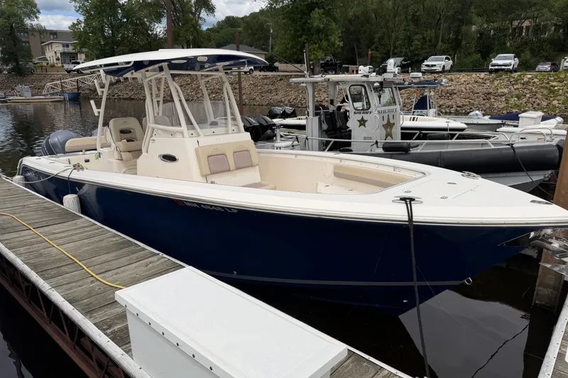 The Image of 2017 Cobia 296 Center Console boat docked at a marina, featuring a sleek blue hull. - 0
