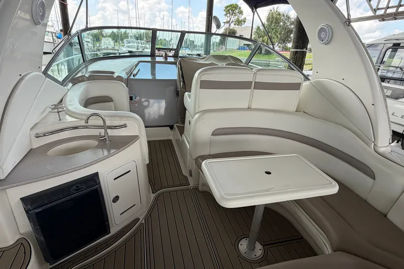 Slide: The Image of 2004 Sea Ray Sundancer 320 interior with seating, table, and kitchenette in a marina setting. - 28