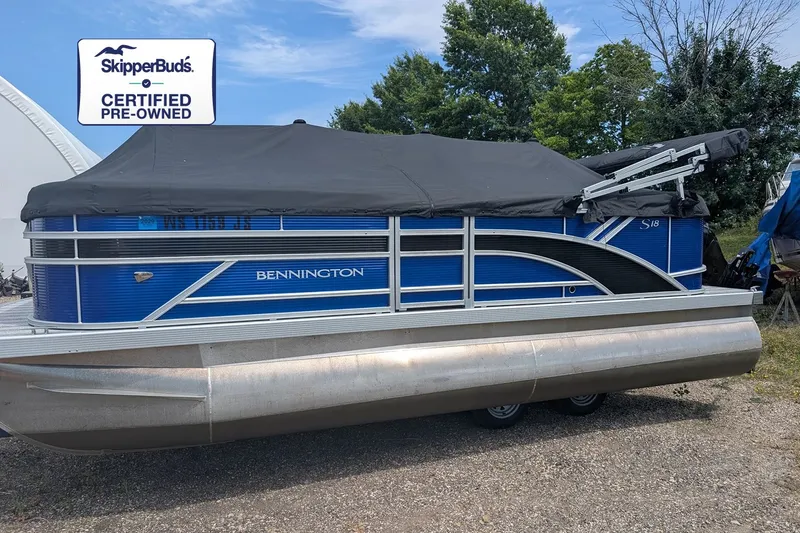The Image of 2025 Bennington S18 pontoon boat with blue siding and black cover, on a trailer. - 0