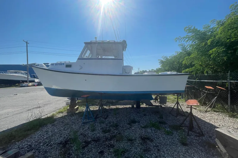 The Image of 1996 Outlaw Marine 25' boat on stands, sunny day, gravel lot, surrounded by trees. - 1