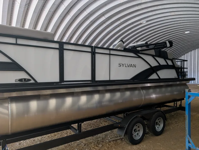 Slide: The Image of A 2026 Sylvan L3 LZ DH pontoon boat is on a trailer in a covered area. - 3