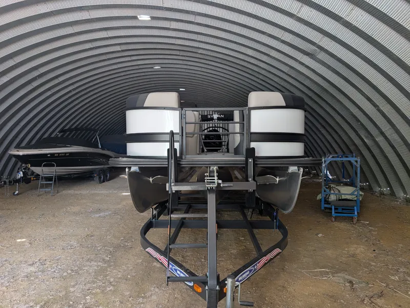 Slide: The Image of A 2026 Sylvan L3 LZ DH pontoon boat is parked in an arched warehouse. - 1
