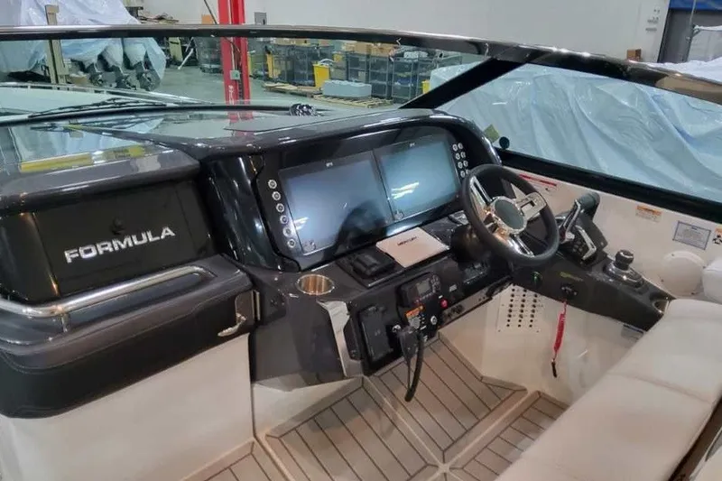 Slide: The Image of Das Bild zeigt das Cockpit eines Formula 360 Crossover Bowrider I/O von 2027. Es verfügt über ein modernes Armaturenbrett mit zwei großen Bildschirmen, einem Lenkrad und verschiedenen Bedienelementen. Die Umgebung wirkt industriell, möglicherweise eine La - 36