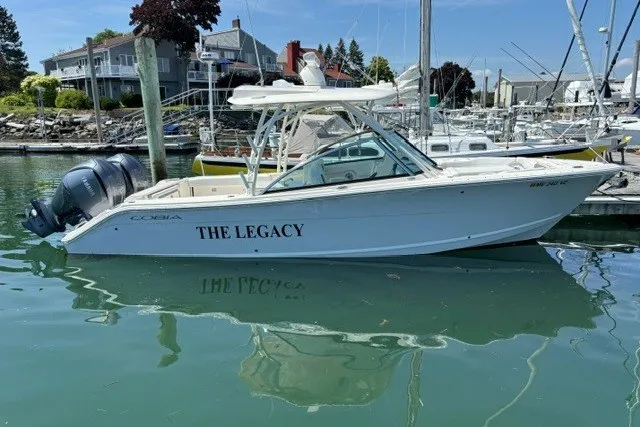Slide: The Image of 2022 Cobia 280 Dual Console boat named "The Legacy" docked in a marina. - 2