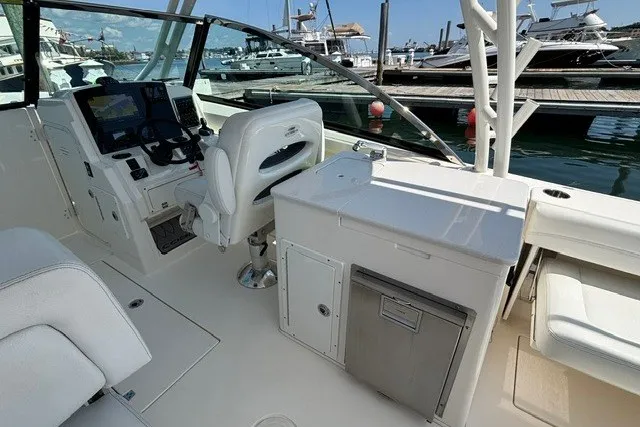 Slide: The Image of 2022 Cobia 280 Dual Console boat interior with helm, seating, and docked marina view. - 11