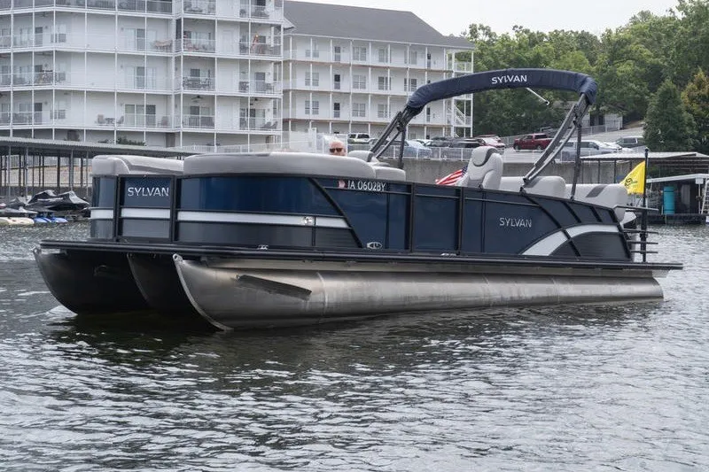 Slide: The Image of 2024 Sylvan L5 DLZ pontoon boat on water near residential buildings. - 2