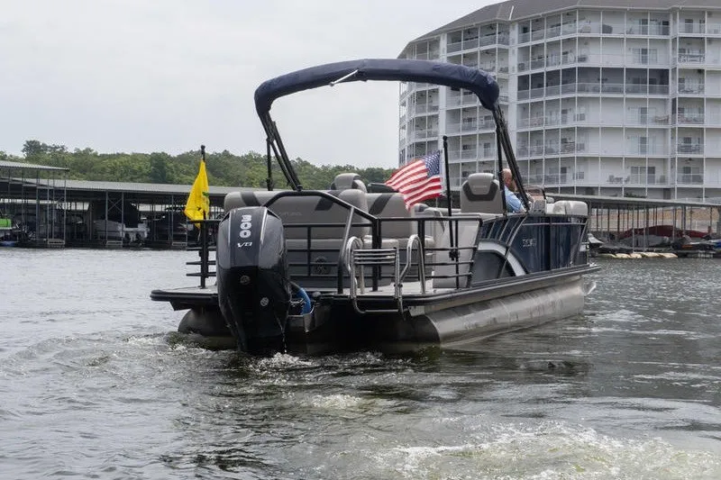 Slide: The Image of 2024 Sylvan L5 DLZ pontoon boat cruising on a lake near a marina. - 4