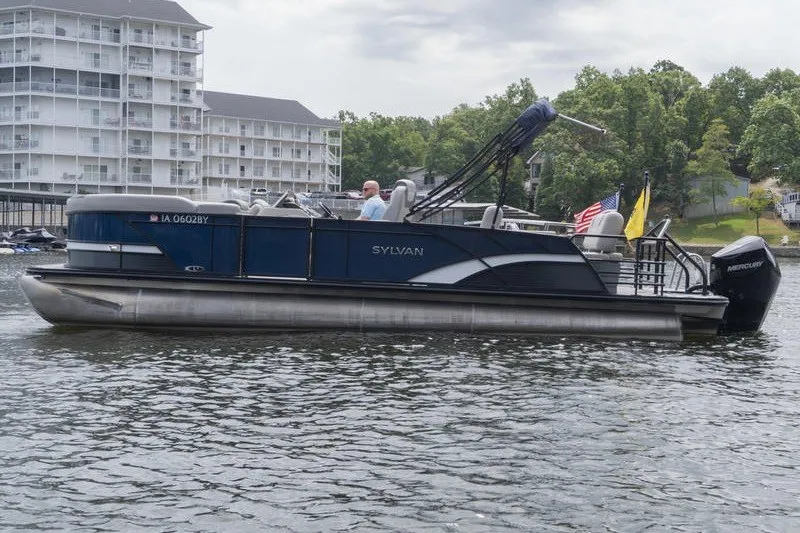Slide: The Image of 2024 Sylvan L5 DLZ pontoon boat on a lake, near waterfront buildings. - 3