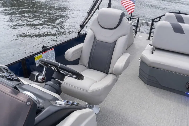 Slide: The Image of 2024 Sylvan L5 DLZ boat interior with plush seating and steering wheel, on calm water. - 24