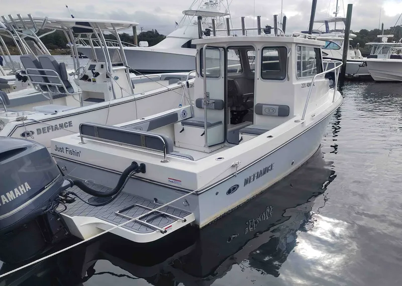 The Image of A 2024 Defiance Admiral 220 EX boat is docked. It features a cabin and an outboard motor. - 0