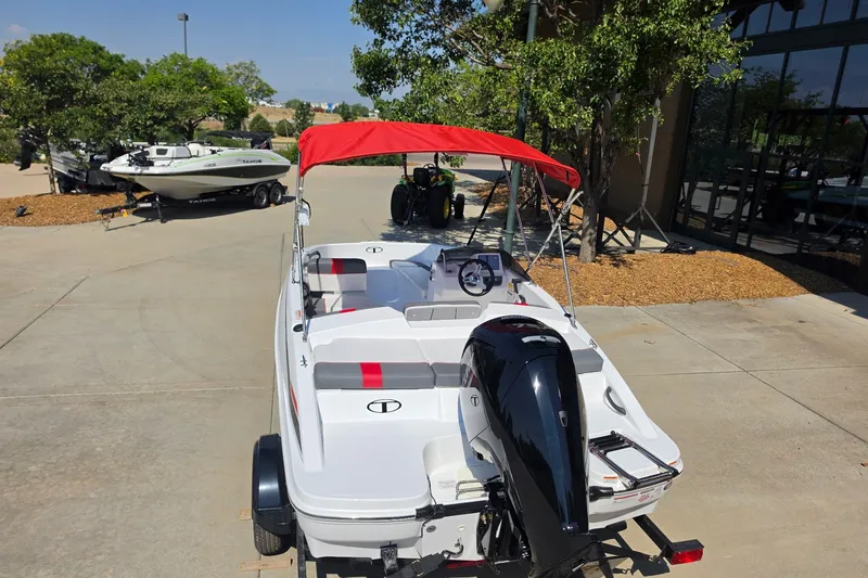 Slide: The Image of 2027 Tahoe T16 boat with red canopy, parked outdoors on a sunny day. - 2