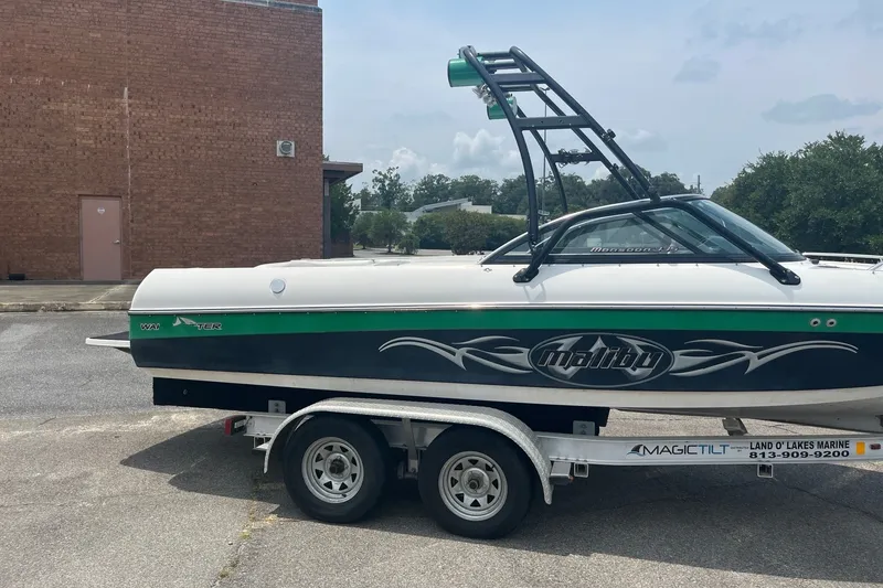 Slide: The Image of 2003 Malibu Wakesetter boat on trailer, parked outdoors near a brick building. - 2