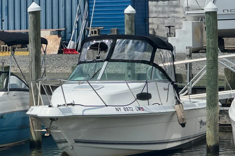 Slide: The Image of 2002 Wellcraft 220 Coastal boat docked at a marina with blue building backdrop. - 1