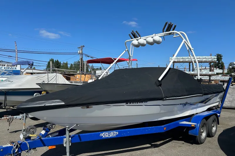 Slide: The Image of 2001 Tige 22i boat on trailer, covered, with wakeboard tower, under clear blue sky. - 1