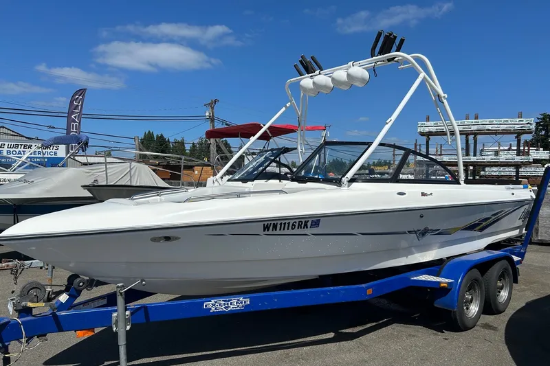 The Image of 2001 Tige 22i boat on a blue trailer, parked outdoors under a clear sky. - 0