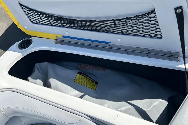 Slide: The Image of Open storage compartment in a 2001 Tige 22i boat, featuring netting and a warning label. - 14