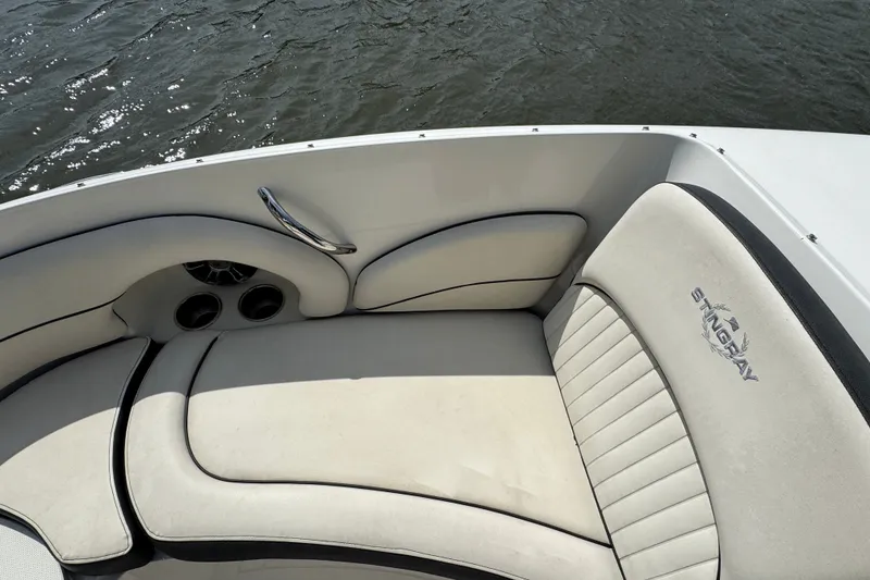 Slide: The Image of 2021 Stingray 214 LR boat interior with cushioned seating and cup holders by the water. - 17