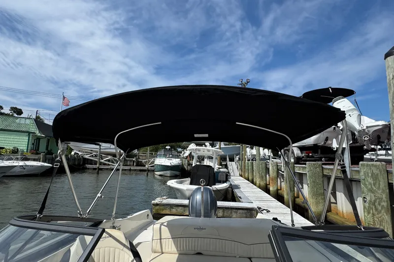 Slide: The Image of 2021 Stingray 214 LR boat docked, featuring a black canopy and beige interior. - 20