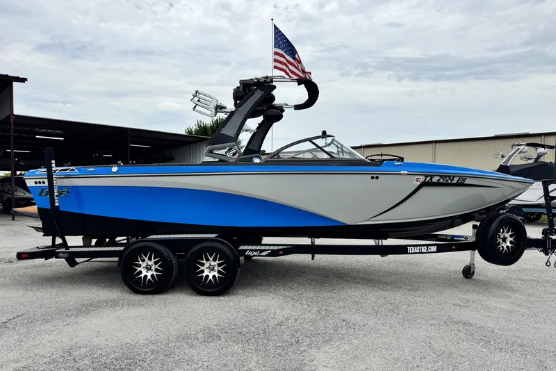 Slide: The Image of 2017 Tigé R23 boat in blue and gray on a trailer, with an American flag. - 2