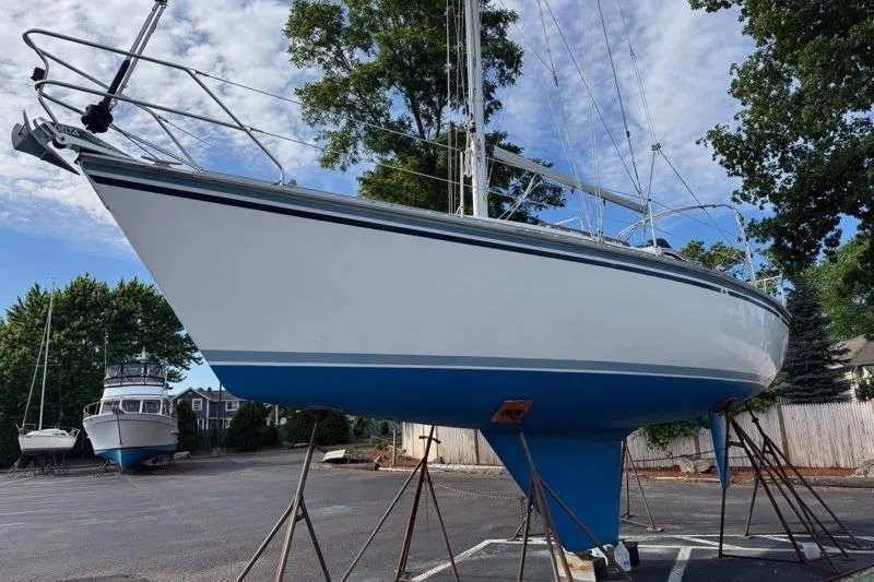 Slide: The Image of 1987 Hunter 31 sailboat on stands in a boatyard, clear sky background. - 20