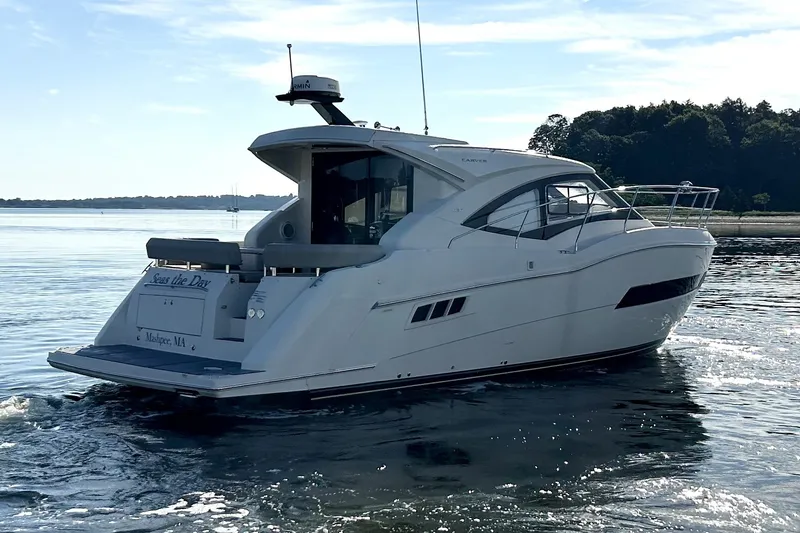 Slide: The Image of 2019 Carver C37 yacht cruising on calm waters near a wooded shoreline. - 2