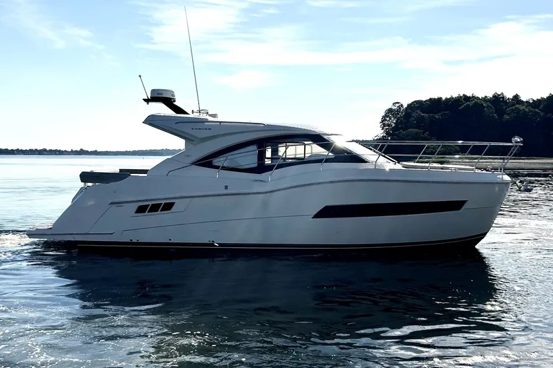 The Image of 2019 Carver C37 yacht cruising on calm waters near a forested shoreline. - 0
