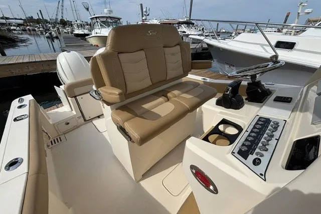 Slide: The Image of 2021 Scout 255 LXF boat interior with tan seating and control panel at marina. - 12