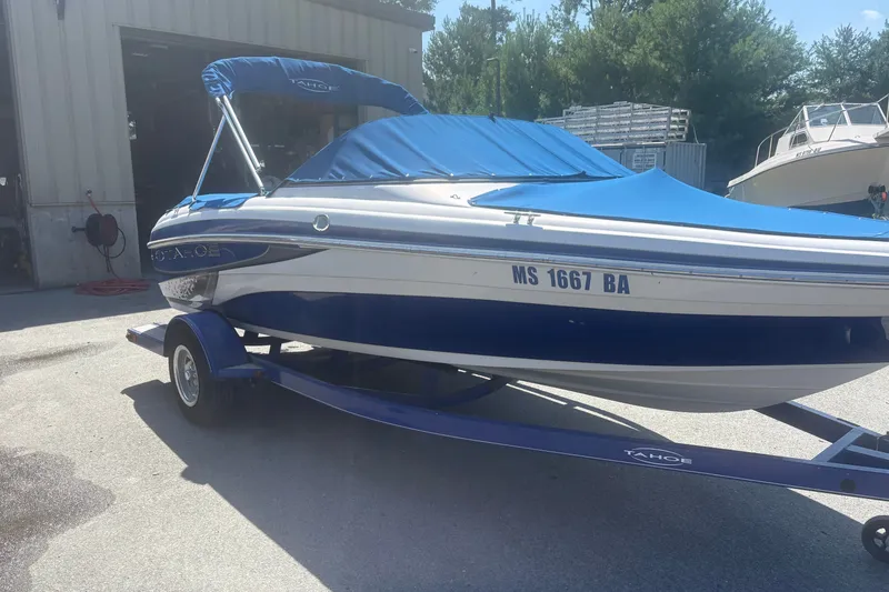 The Image of 2011 Tahoe Q4 SF boat with blue cover on trailer, parked outdoors. - 0